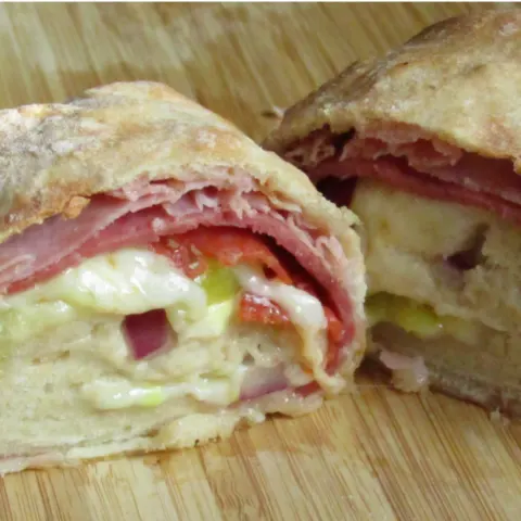 Stromboli cut in half showing the fillings on a wooden cutting board