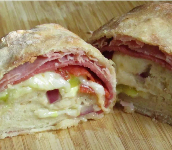 Stromboli cut in half showing the fillings on a wooden cutting board