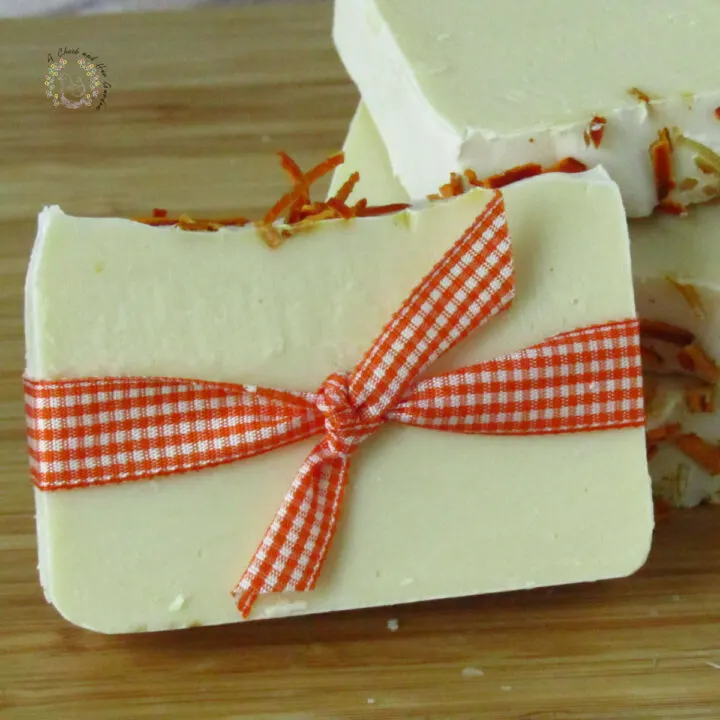 one bar of white soap with dried orange peels on top wrapped in orange gingham ribbon leaning against three stacked bars of soap