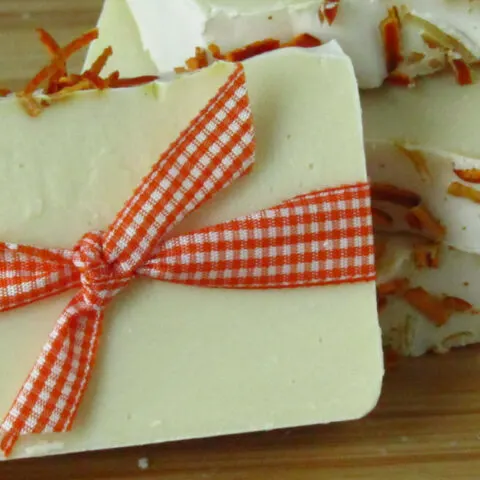 one bar of white soap with dried orange peels on top wrapped in orange gingham ribbon leaning against two stacked bars of soap