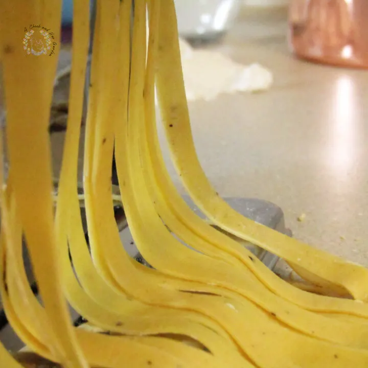 fresh pasta hanging from a pasta maker with a copper measuring cup and flour in the background