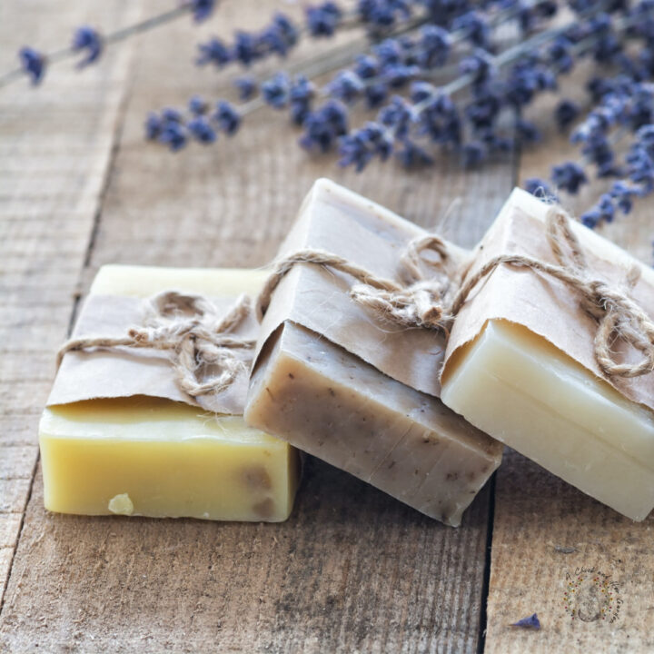 three bars of artisan soap wrapped in paper and twine on a wooden surface with lavender in the background