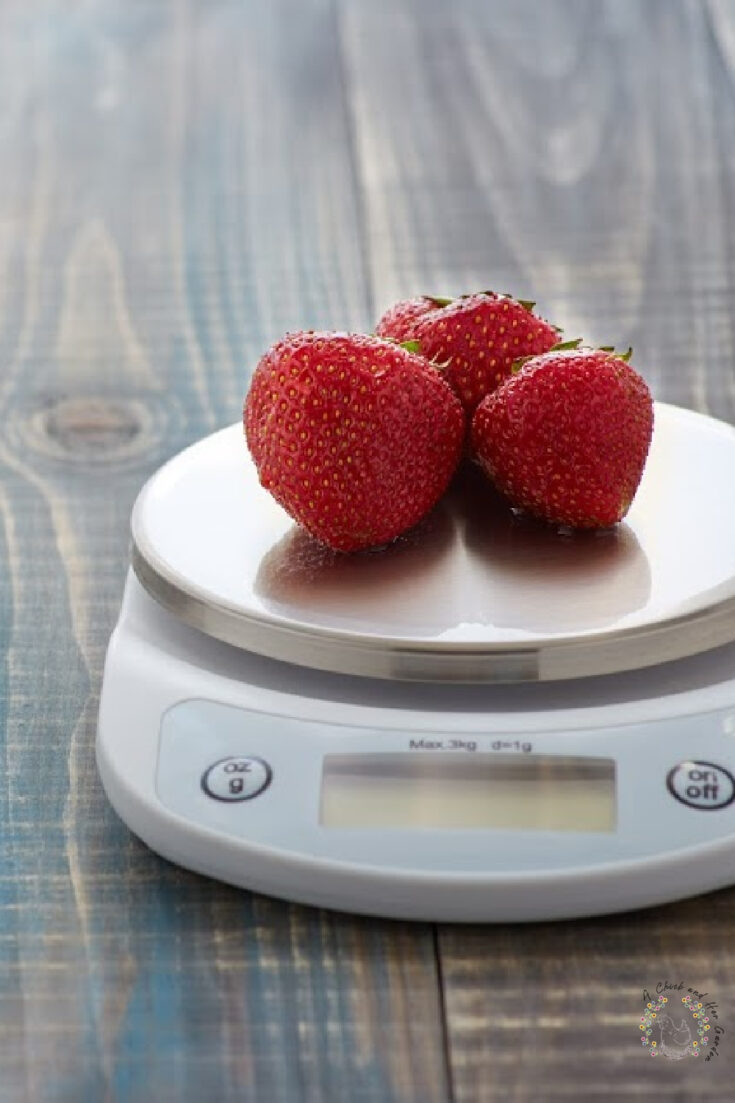 Three ripe strawberries sitting on electronic kitchen scale on a wooden surface