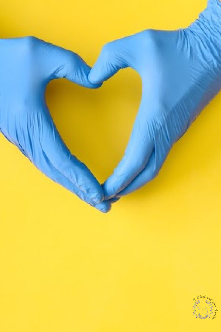 Hands in blue medical gloves showing shape of heart on yellow background