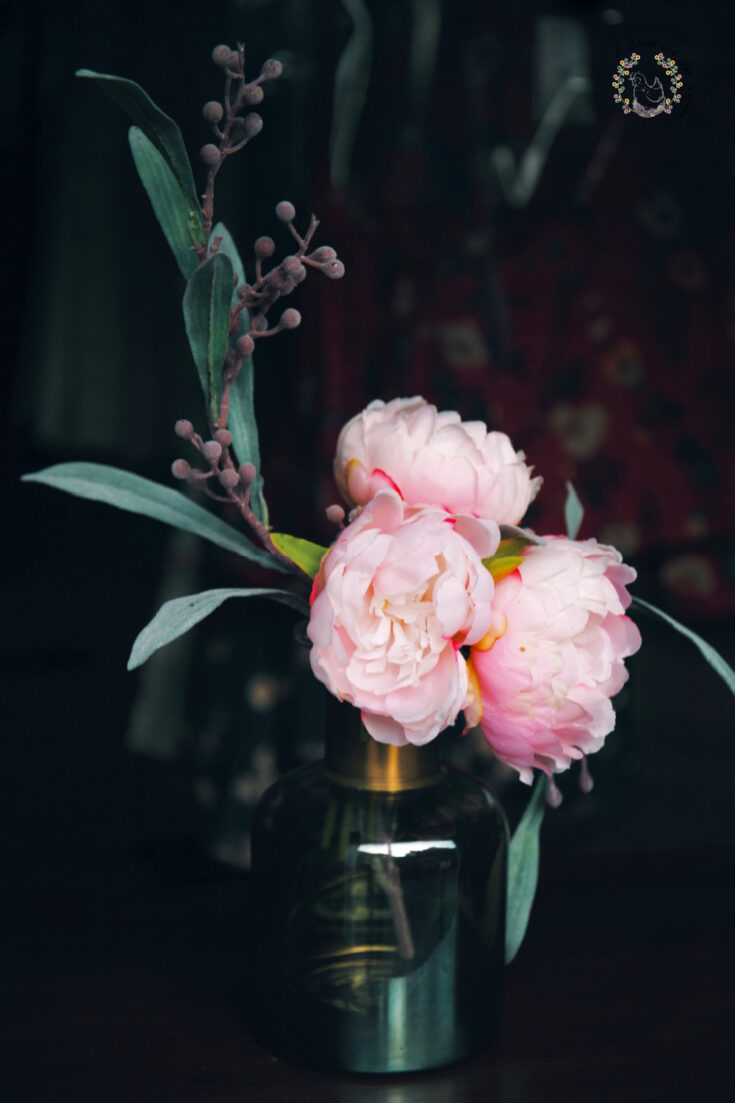 three pale pink peony flowers with seeded eucalyptus in a small glass vase