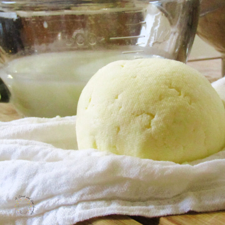 ball of fresh butter sitting on cheesecloth with a bowl of whey in the background