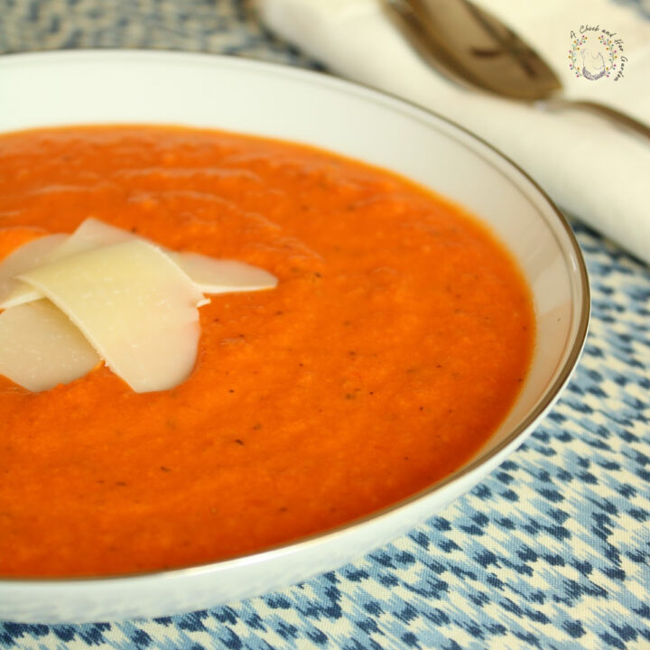 tomato soup in a white bowl on a blue and white placemat with shaved parmesan on top