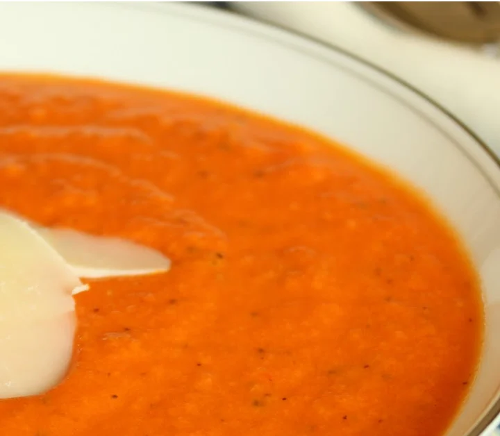 tomato soup in a white bowl on a blue and white placemat with shaved parmesan on top