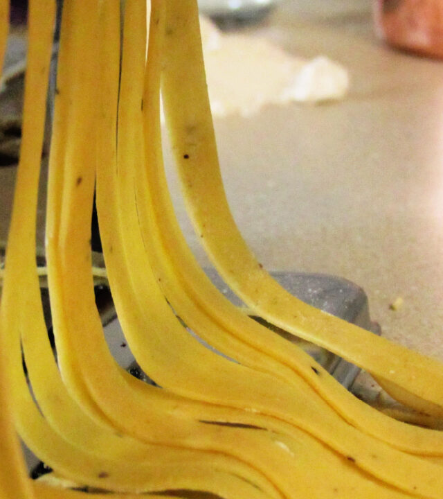 fresh pasta passing through a pasta maker with a copper measuring cup and flour in the background