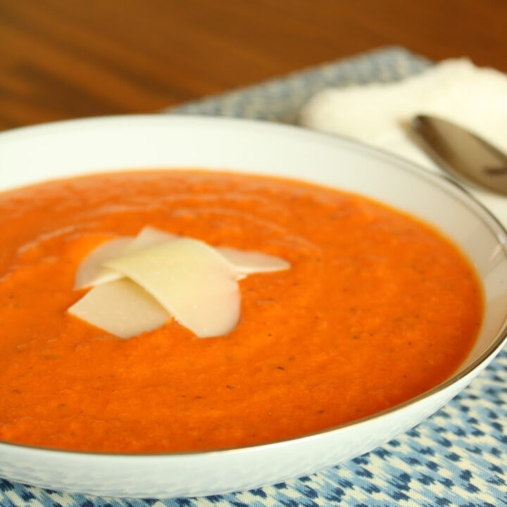 close up of tomato soup in a white bowl with parmesan shavings on top