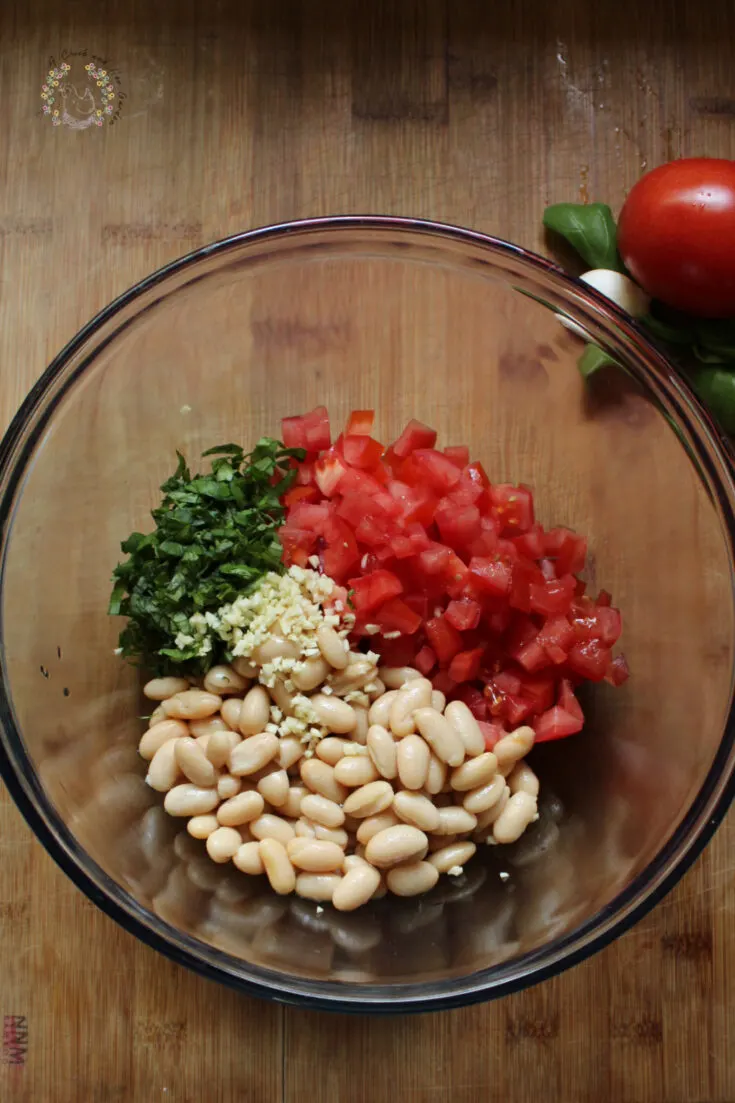 glass bowl with diced tomatoes, cannellini beans, chopped basil and minced garlic