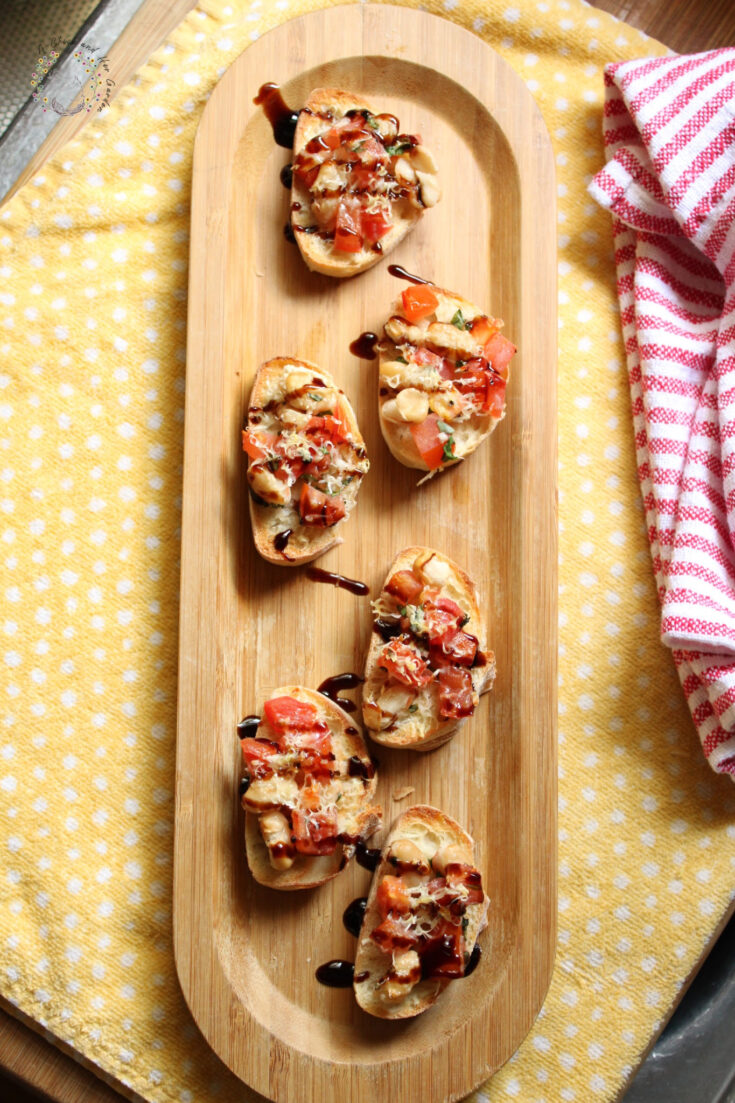 six baguette slices topped with bruschetta and drizzled with balsamic reduction on a bamboo tray