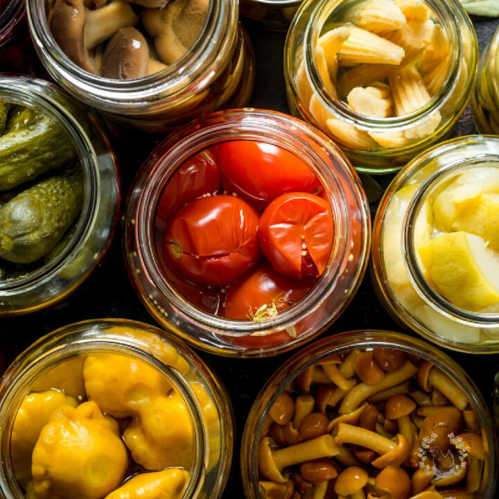 overhead view of glass jars filled with tomatoes, pickles, baby corn, squash and mushrooms